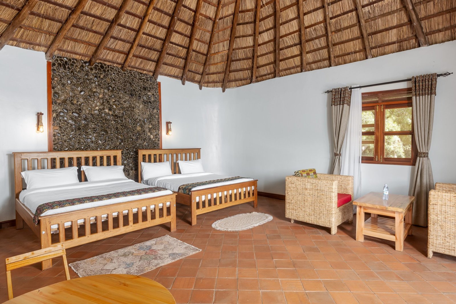 Two king size beds beneath the double cottage thatched roof at Bahundu near Fort Portal