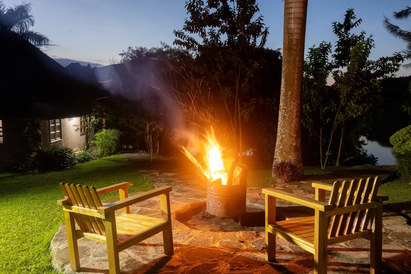 An open fire burning in the garden firepit with chairs drawn around it after dark
