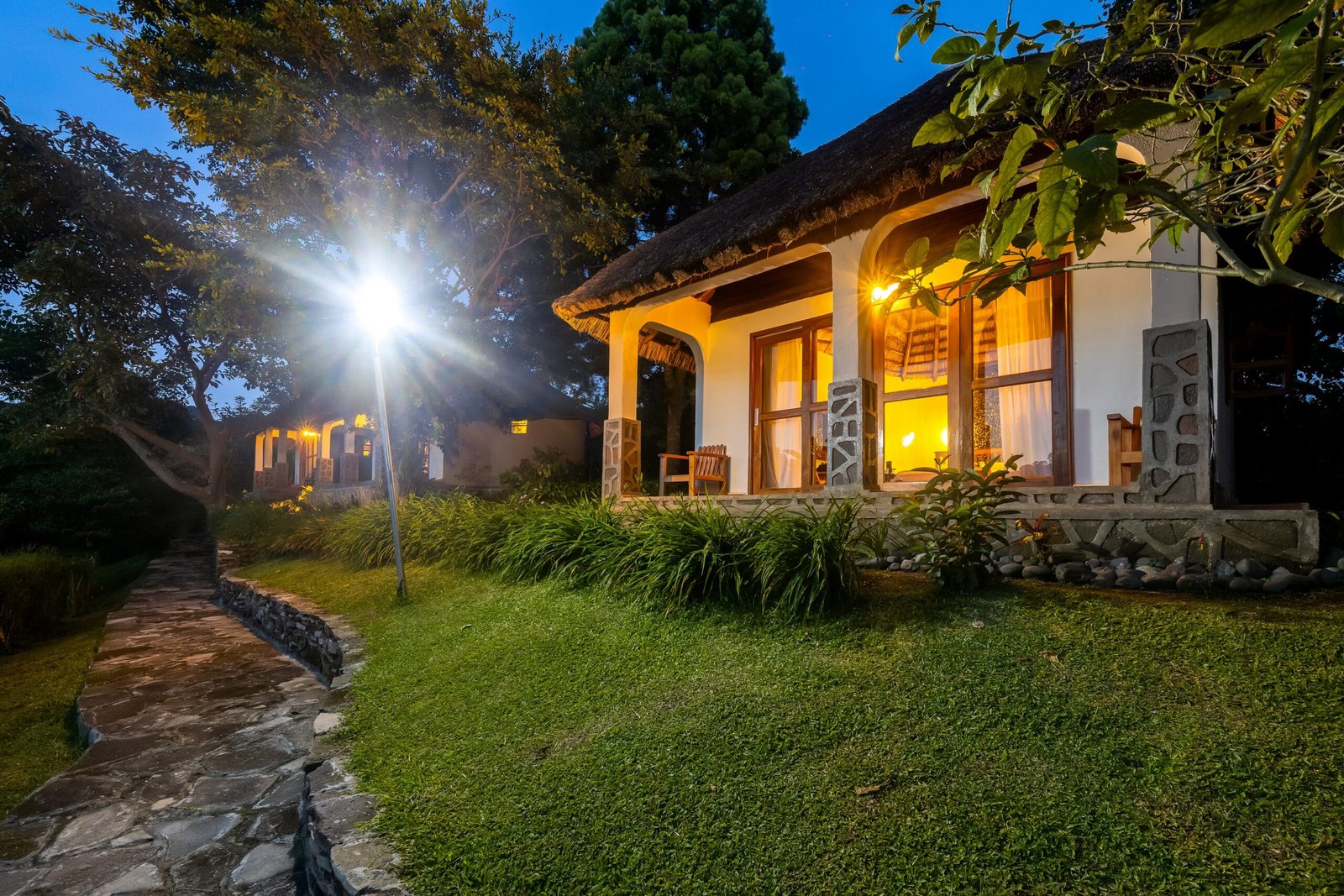 Thatched cottage glowing softly in the silent lodge gardens at night at Bahundu in western Uganda, East Africa