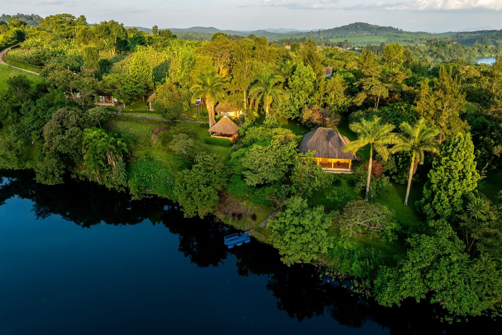 Thatched cottages catching low golden light above the crater lake at Bahundu near Fort Portal, Uganda