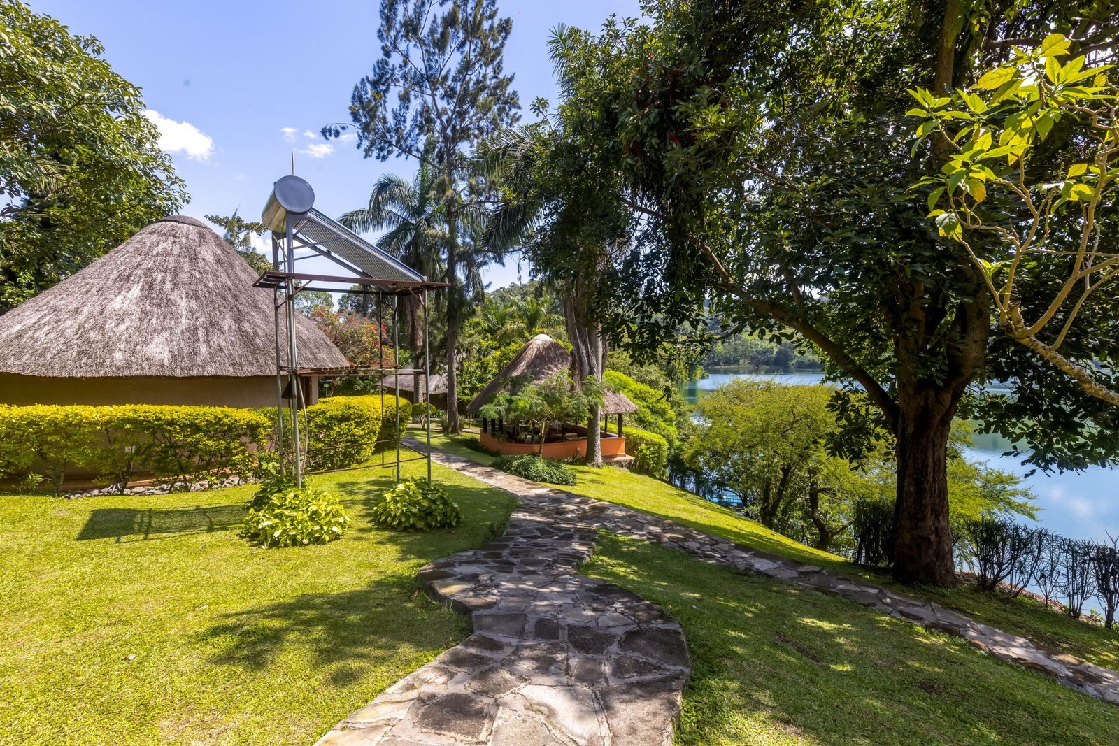 A round thatched cottage on the lawn with a stone path and the lake beyond