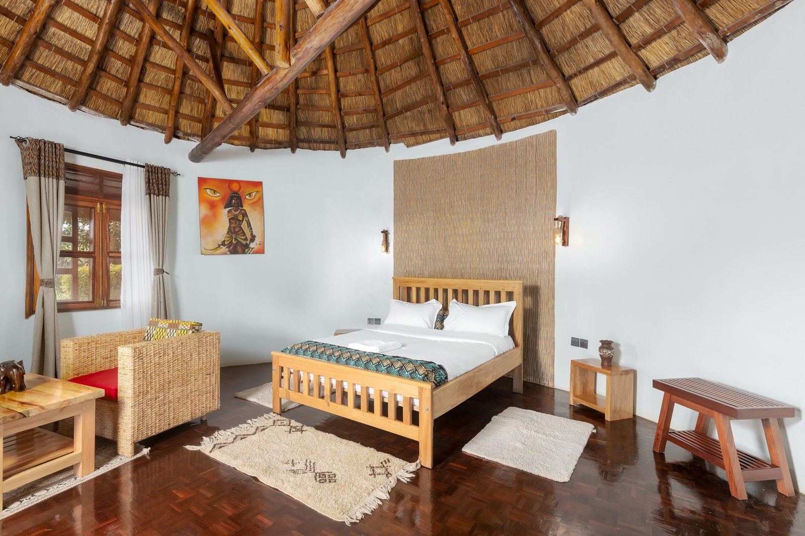 A king cottage bed beneath the round thatched roof, with woven furniture and local artwork